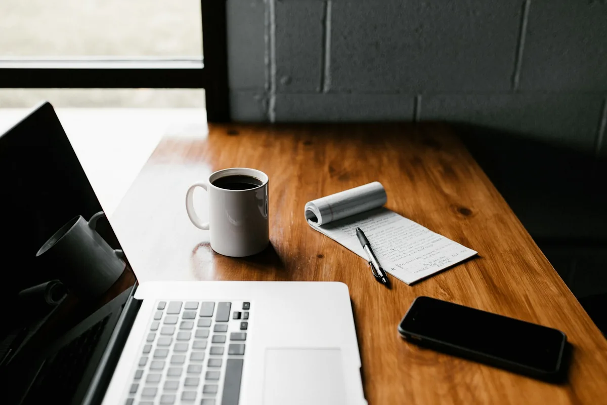 Distraction-free minimalist wooden desk with a single open paper journal, ceramic tea cup and peaceful morning window light